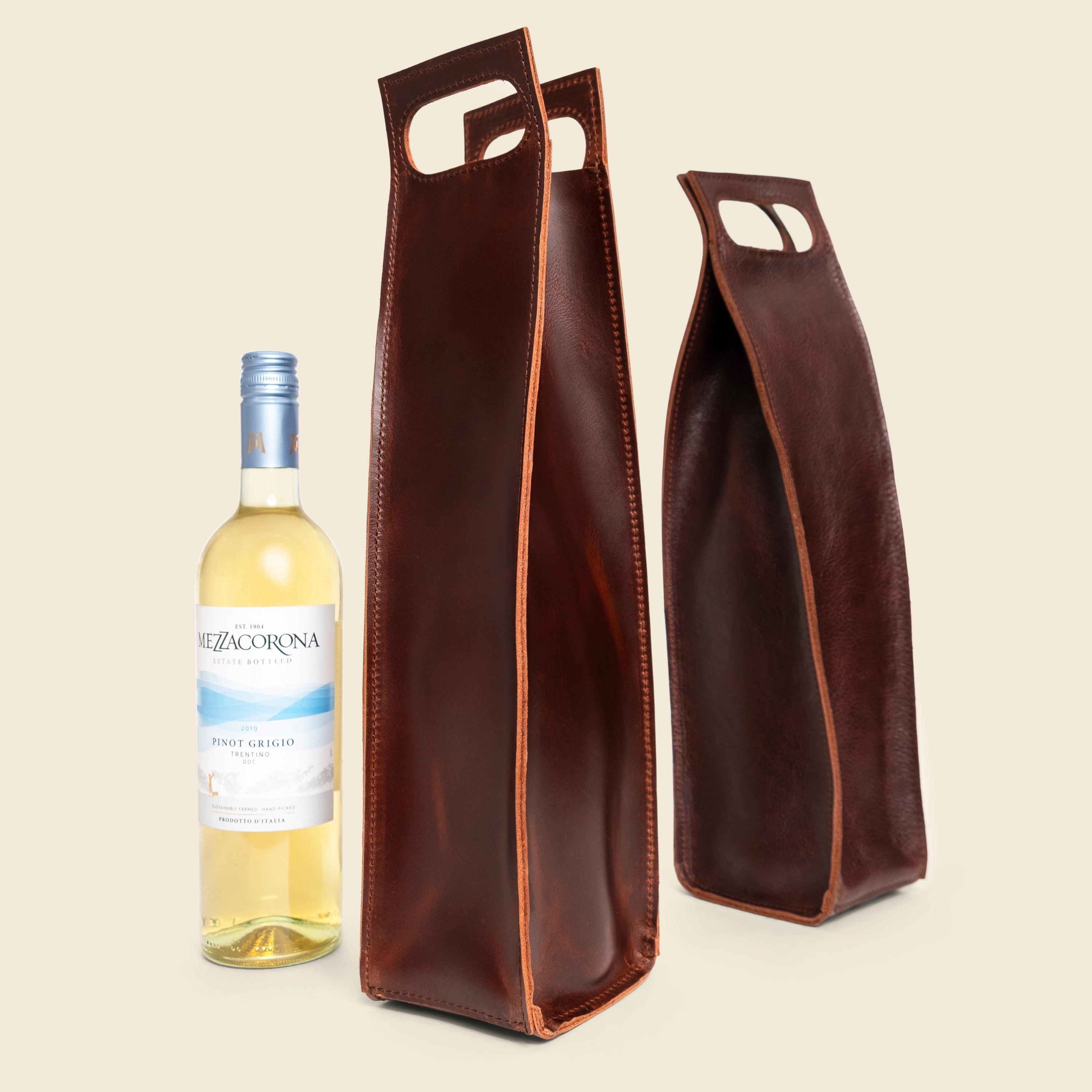 Two brown leather wine bottle holders with a white wine bottle on a beige background