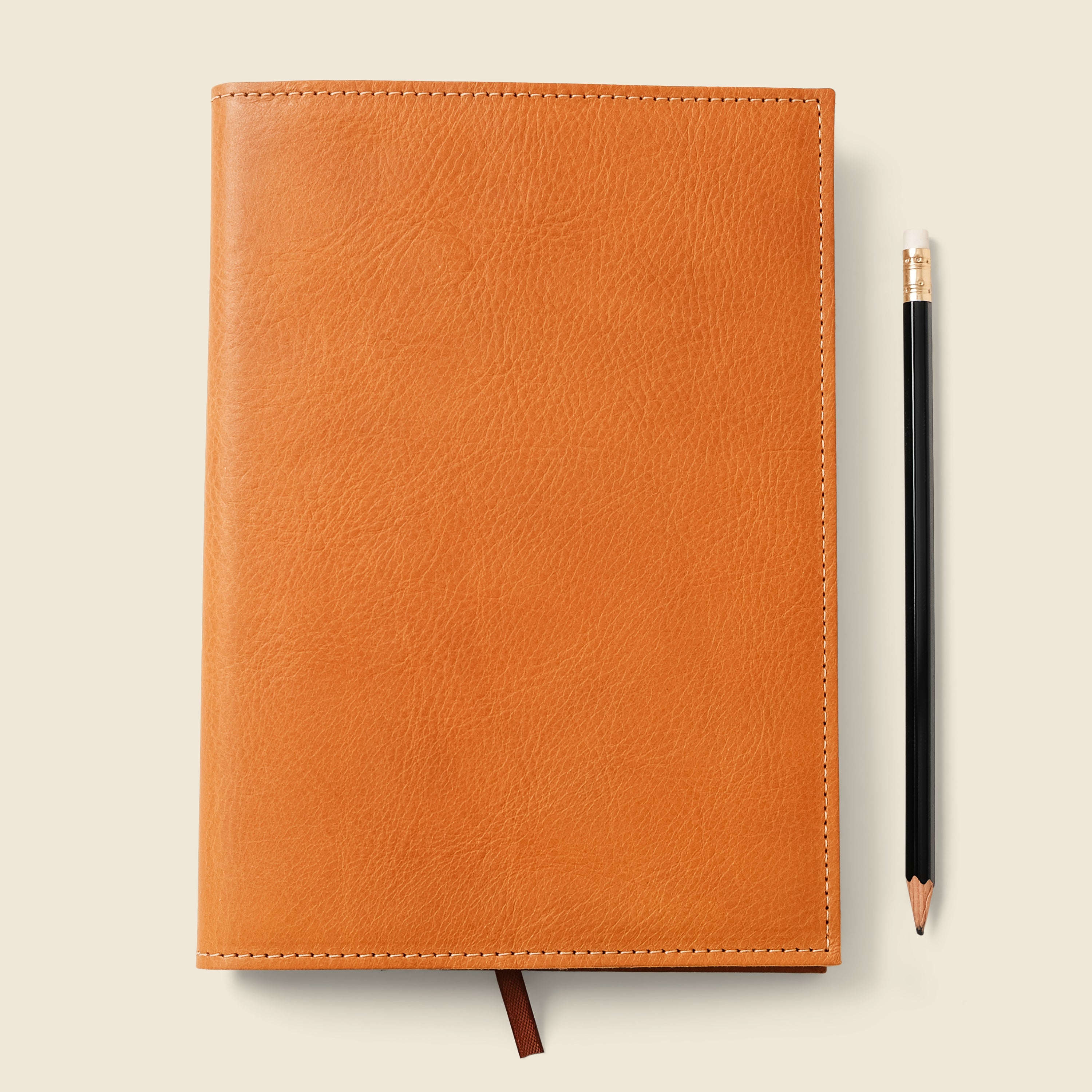 Orange leather notebook with a pencil on a beige background