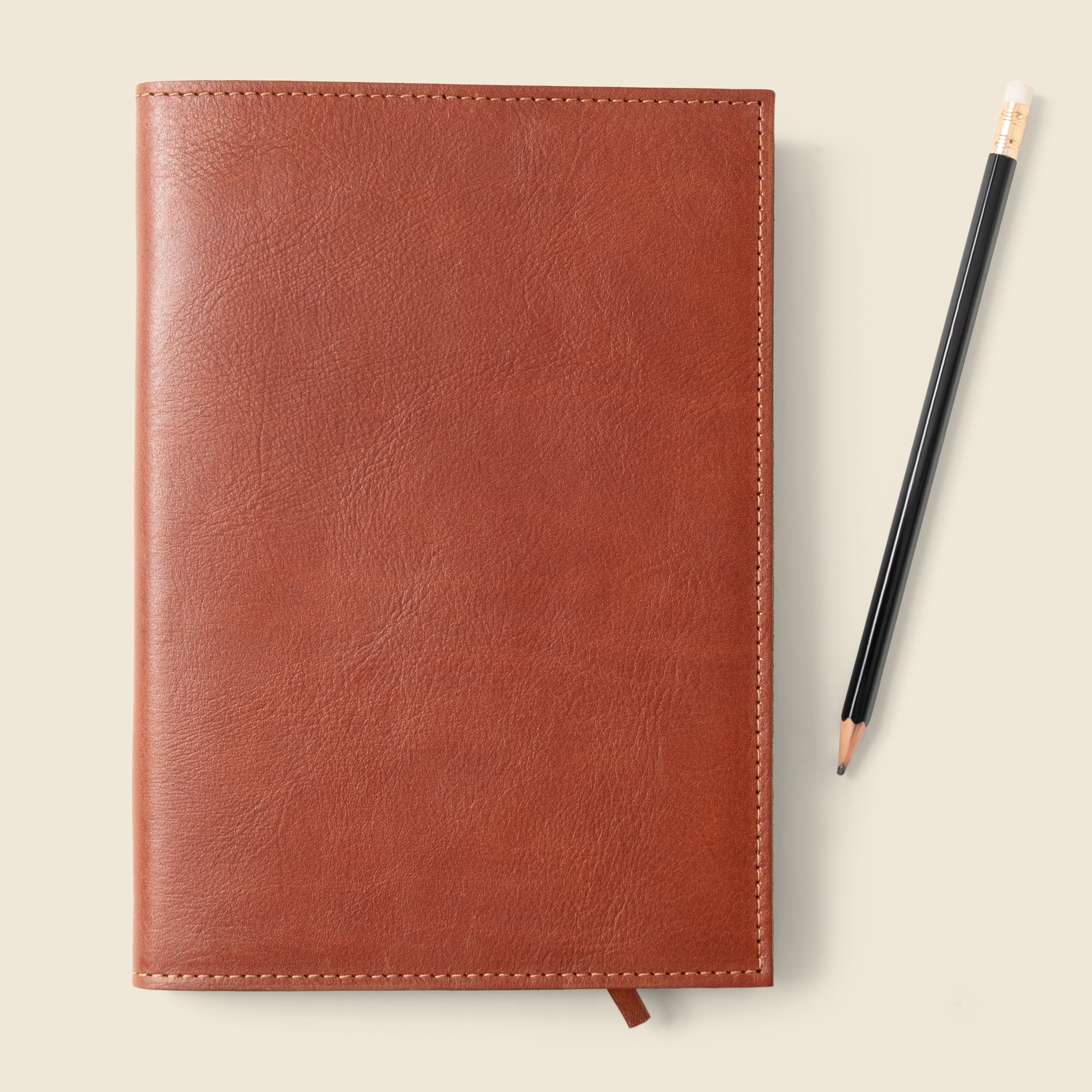 Brown leather notebook with a pencil on a light beige background