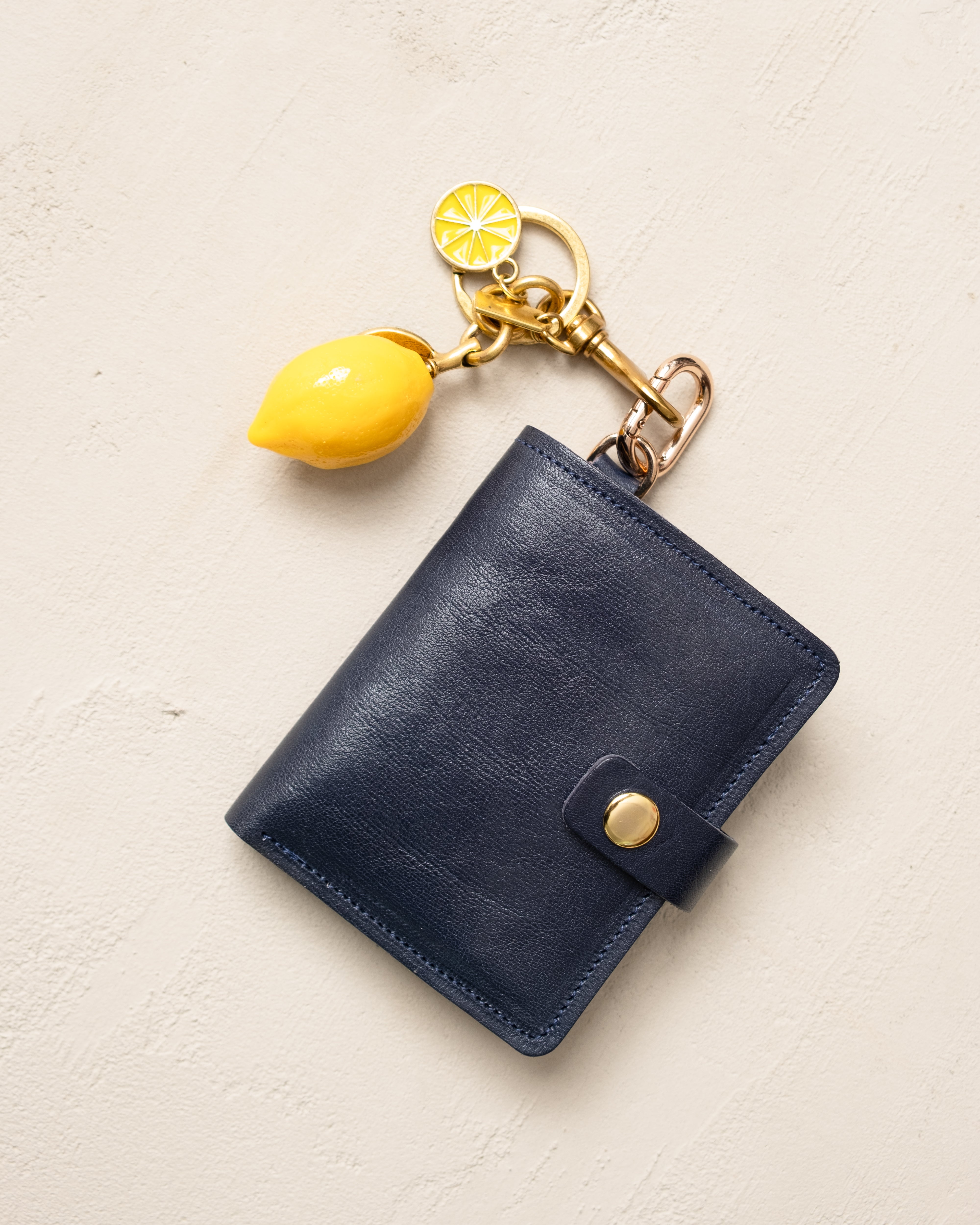 Blue leather wallet with a yellow lemon-shaped keychain on a light beige background