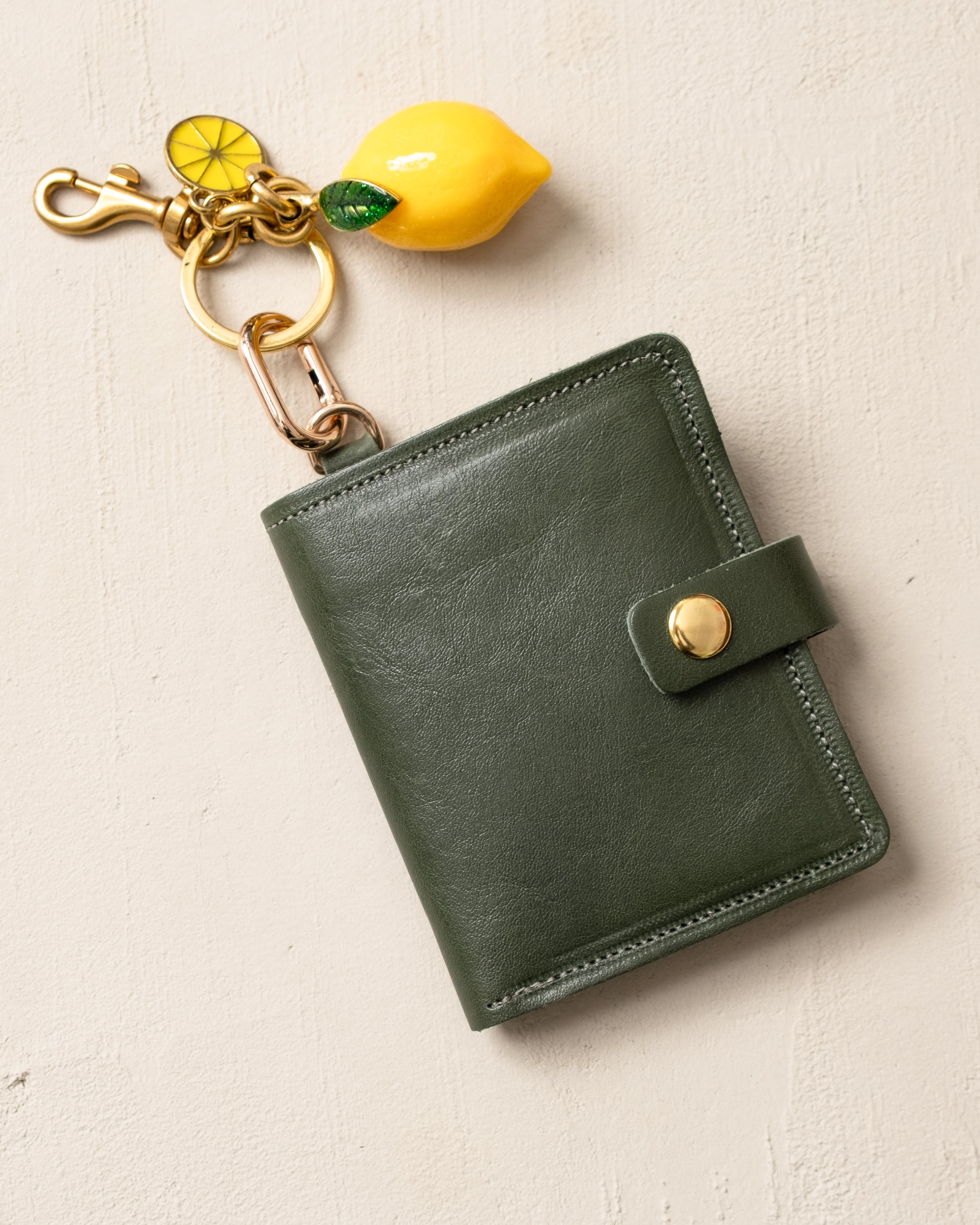 Green leather wallet with a lemon-shaped keychain on a beige background