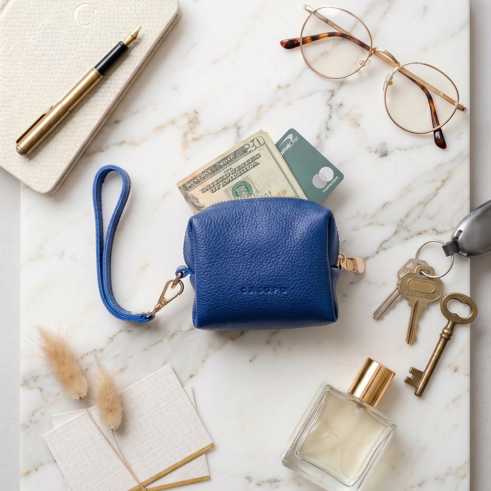 Blue leather wallet on a marble surface with various items including keys, glasses, and a pen.