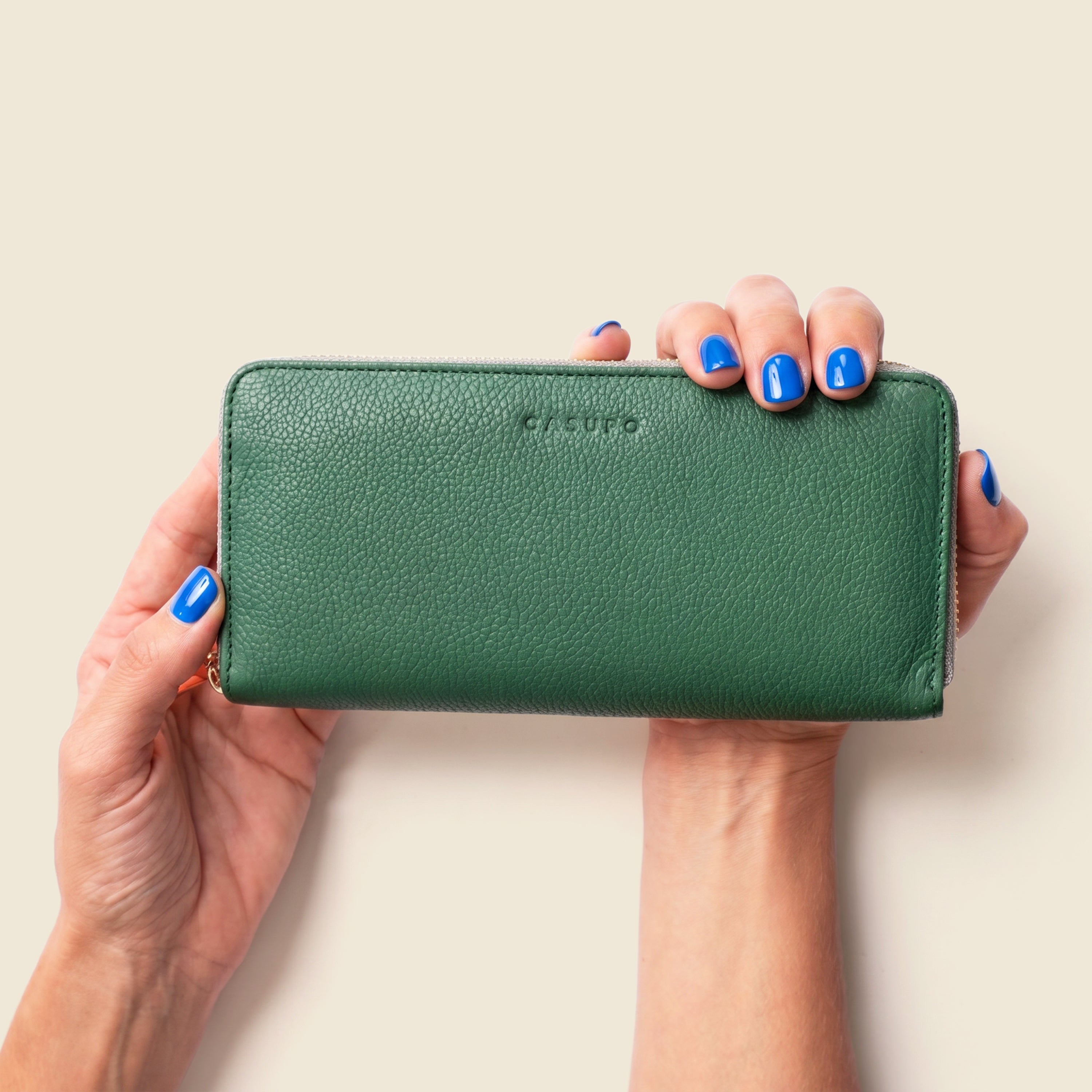 Green wallet held by hands with blue nail polish on a beige background