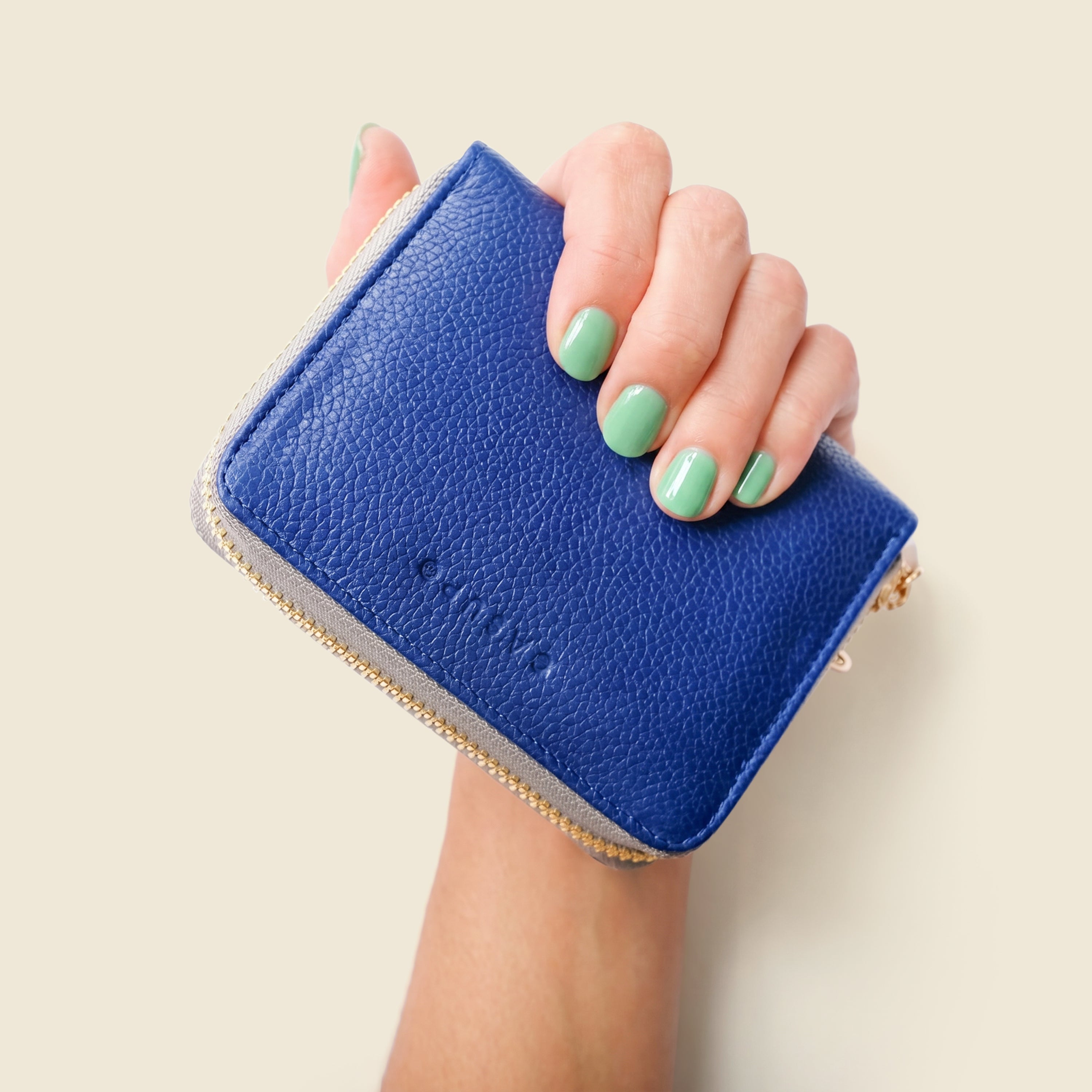 Hand holding a blue wallet against a beige background
